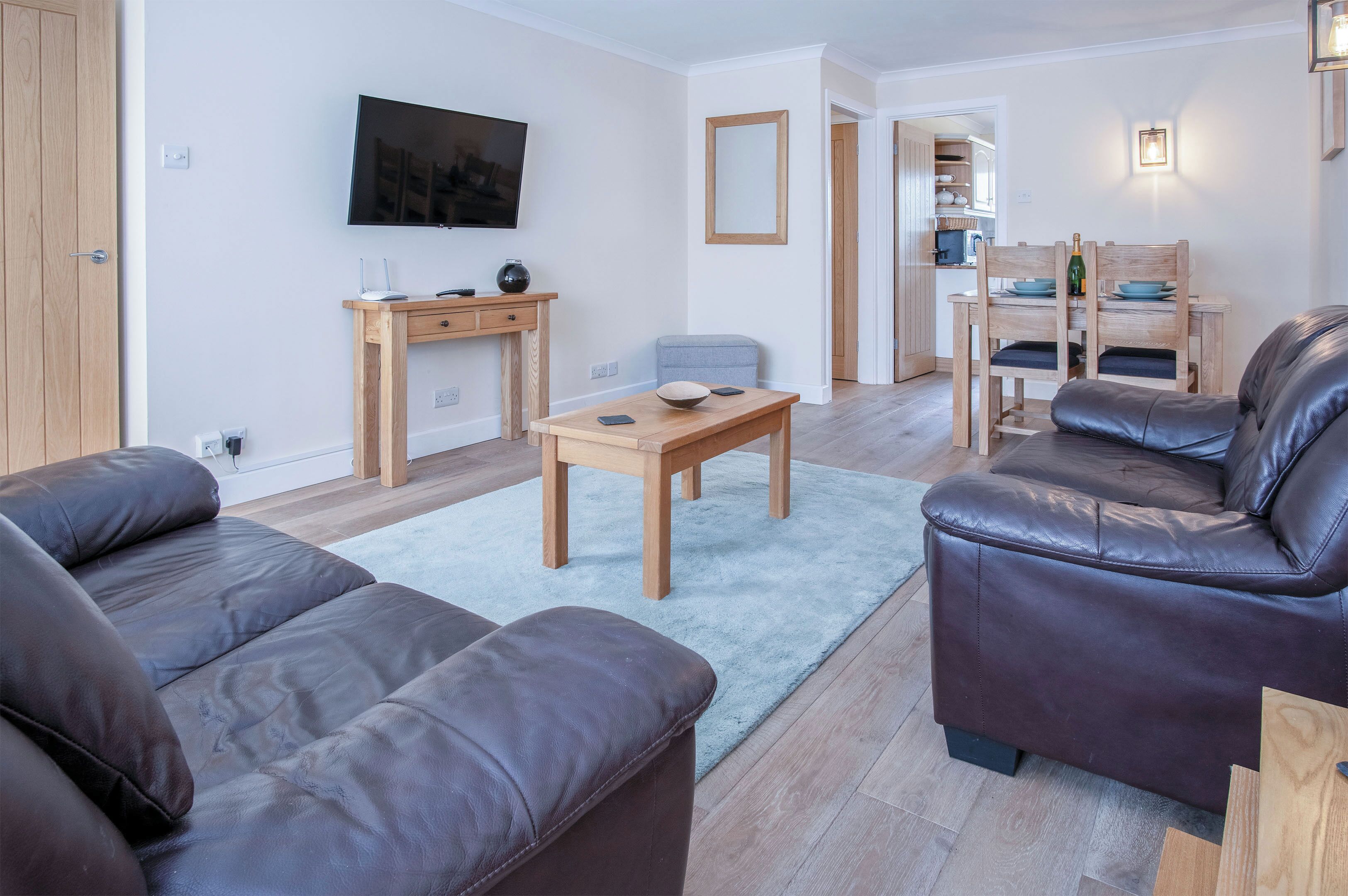 Ein modernes Wohnzimmer mit einer Ledersofa, einem Holztisch und einem an der Wand befestigten Fernseher.