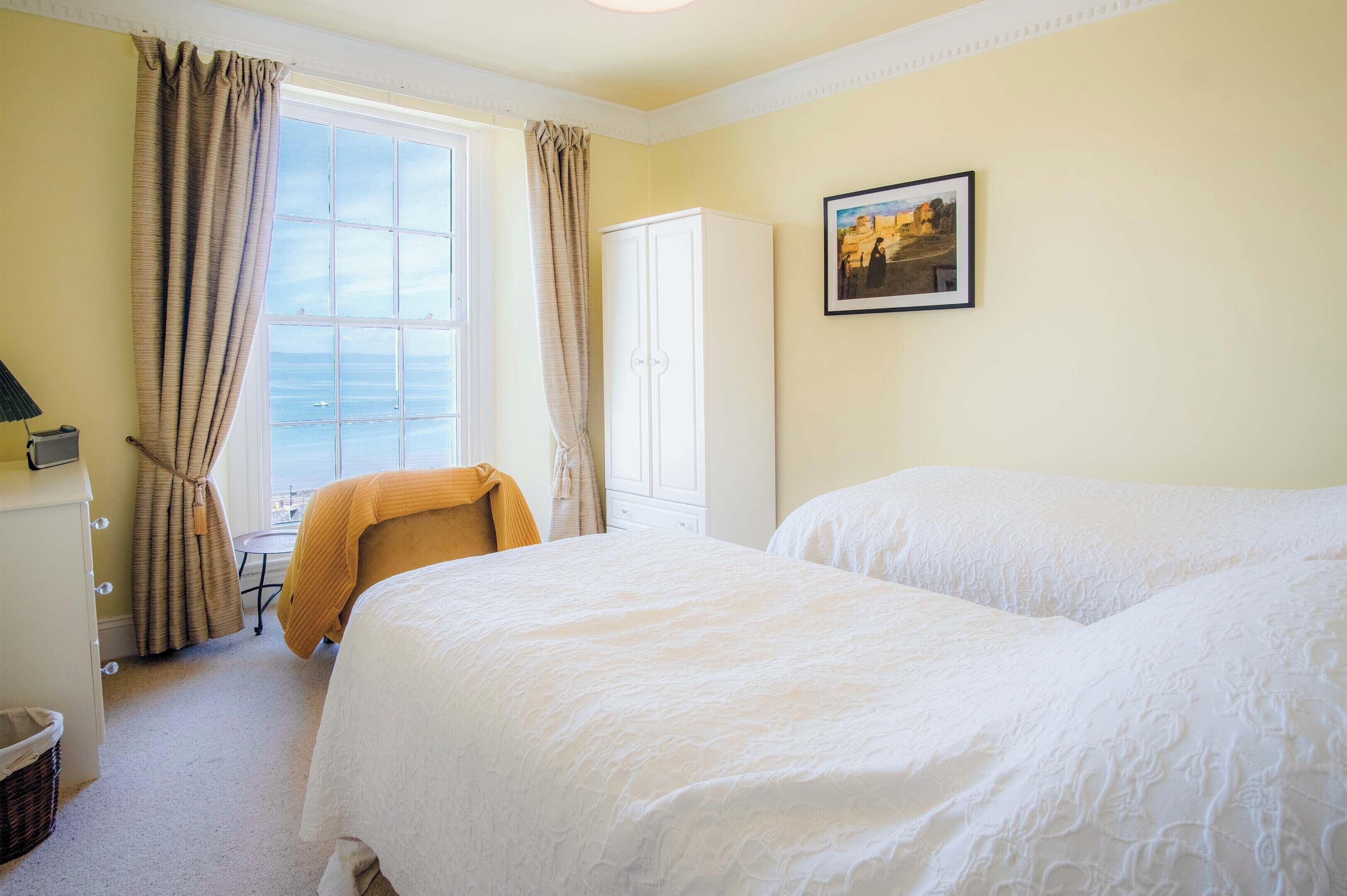 A hotel room with two beds, a window with curtains, a wardrobe, and a framed picture on the wall.