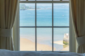 A view through a window with a view of the sea, a sandy beach, and a stone structure. - 5 Belle Vue Court - 2 Bedroom Apartment - Tenby (Tenby)