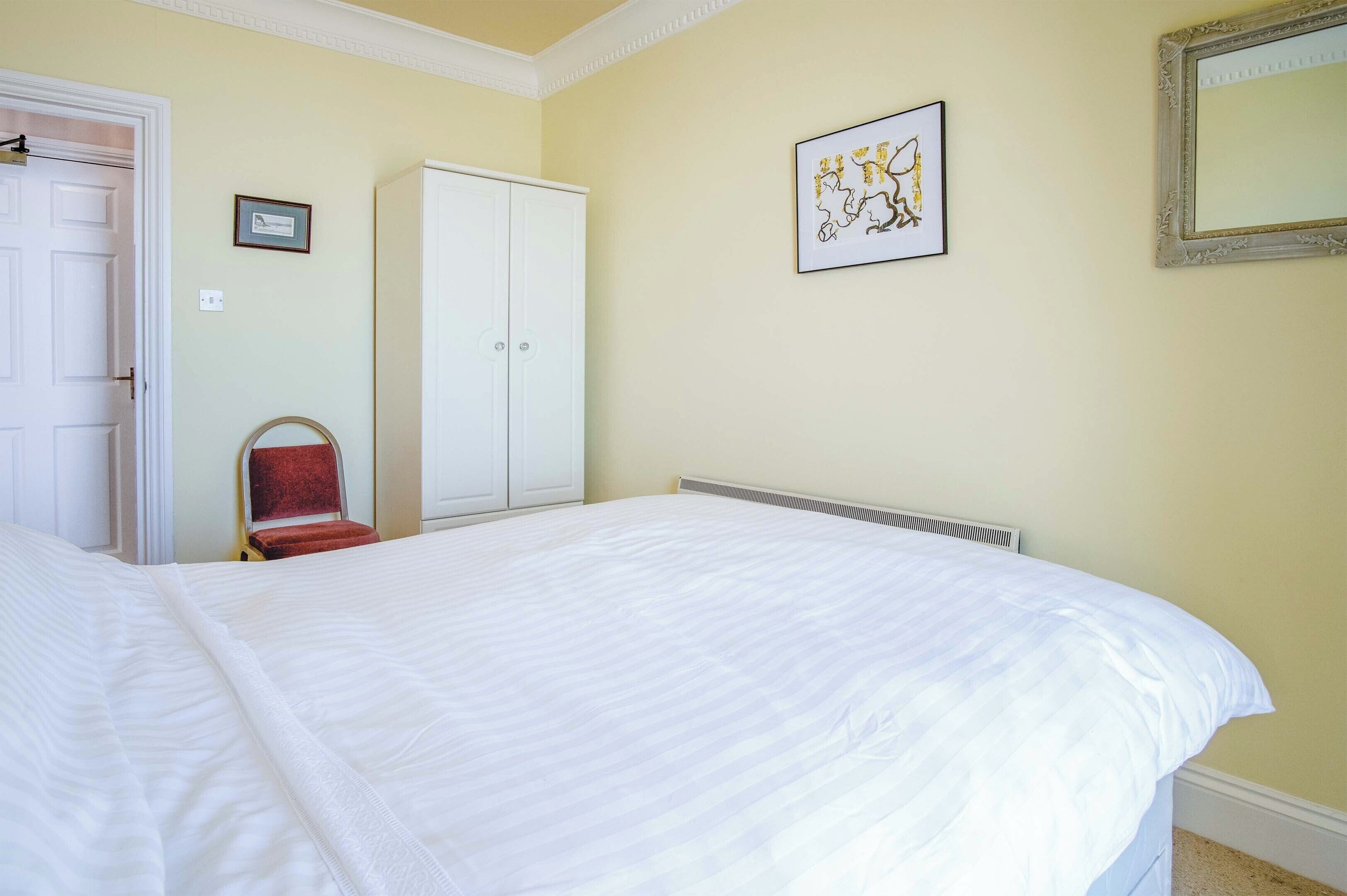A bedroom with a large bed, a wardrobe, a chair, and a framed picture on the wall.