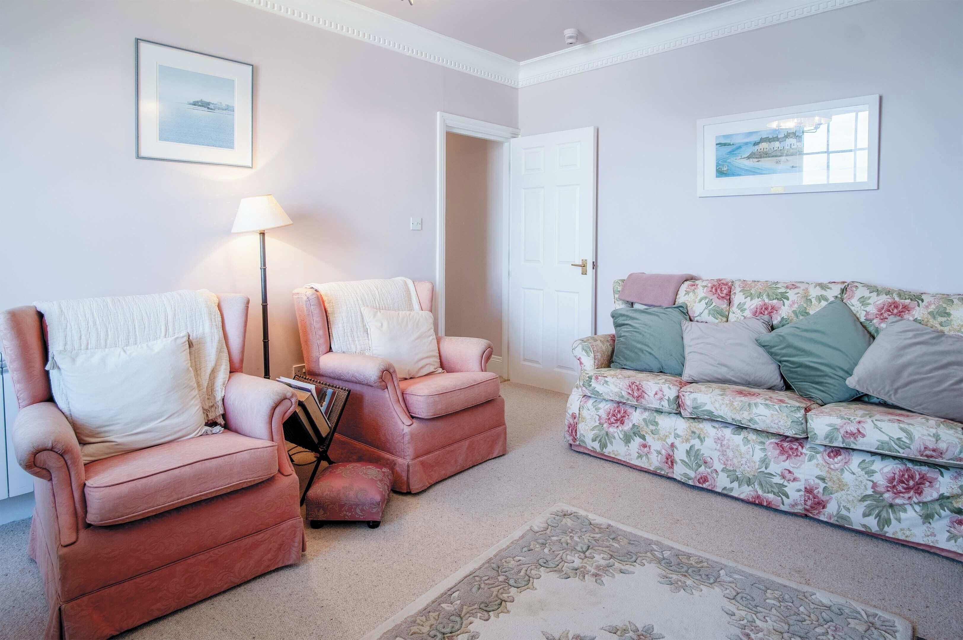 Un salon avec deux fauteuils roses, un canapé à motifs floraux et un lampadaire.