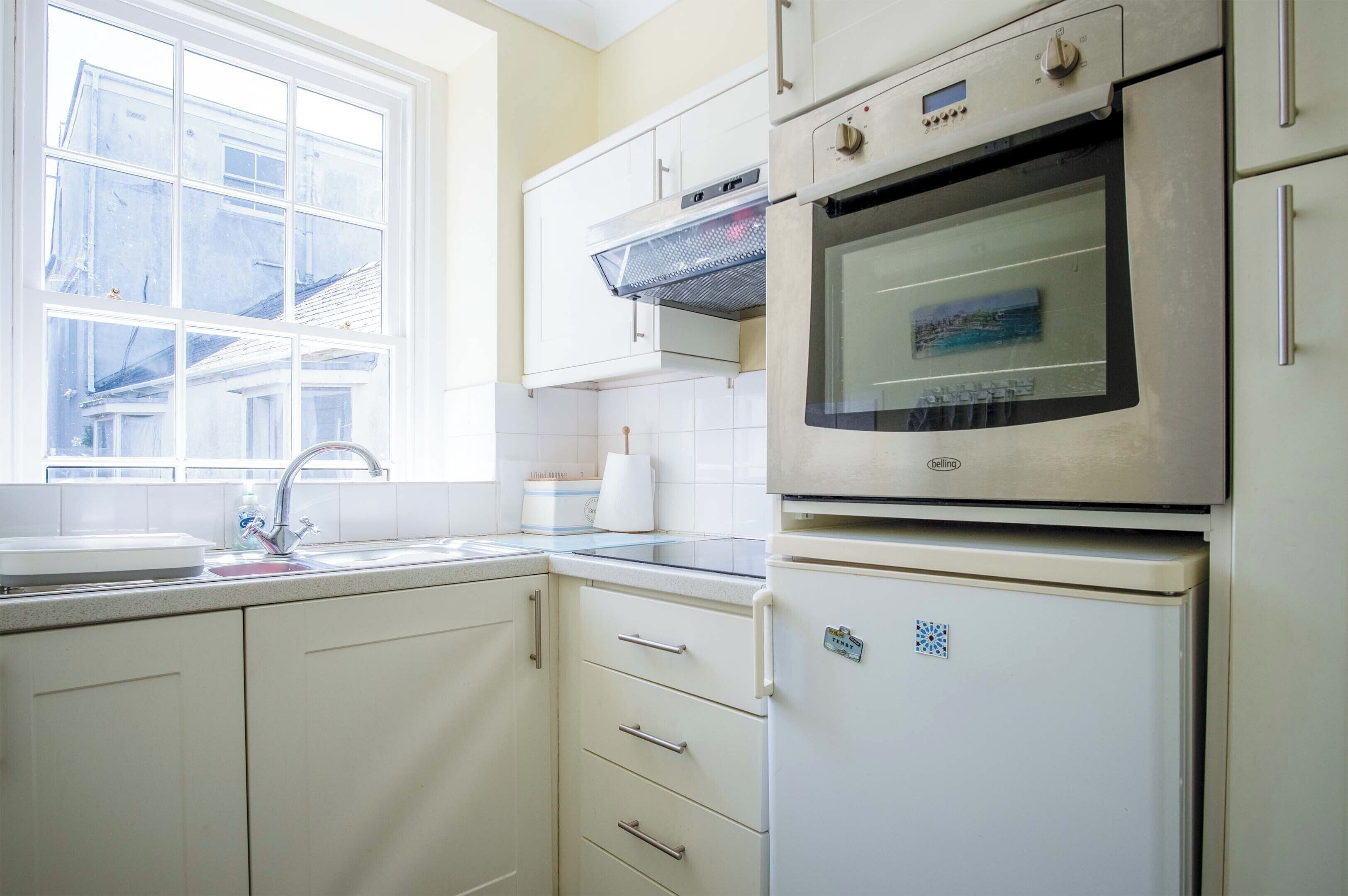 A kitchen with white cabinets, a double oven, a sink, and a window.