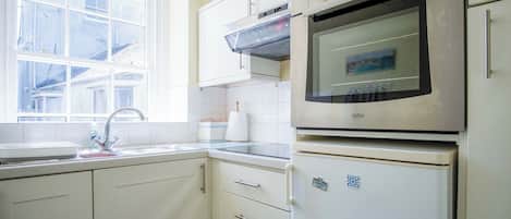 A kitchen with white cabinets, a double oven, a sink, and a window.