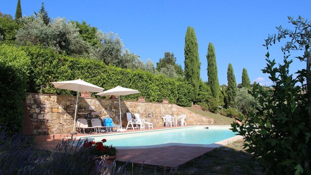A pool with lounge chairs and umbrellas, surrounded by stone walls and greenery. - Villa Amaranto Summar (Tuscany)