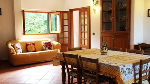 A dining area with a table set for four, a yellow sofa with floral cushions, and a cabinet with glass doors. - Villa Amaranto Summar (Tuscany)
