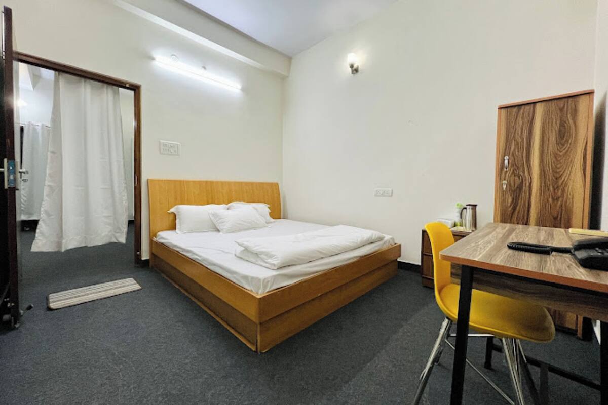 Una cama individual con cabecera de madera, una mesita con una silla y un armario.