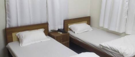A hotel room with two single beds, a wooden headboard, a nightstand, and a wall-mounted air conditioner.