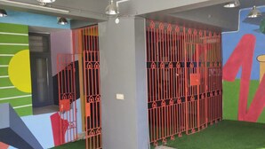 Una habitación con césped artificial, un mural colorido y una reja de metal roja.