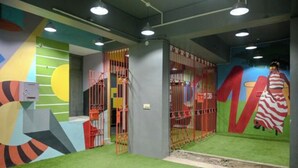 Zona de juegos con murales coloridos, suelo acolchado y estructura delimitada por una cerca.