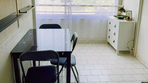 Ein kleiner, sauberer Raum mit Esstisch, zwei Stühlen, einem weißen Schrank und einem Fenster mit Blick auf Gebäude.