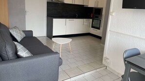 Ein gemütlicher Wohnbereich mit grauem Sofa, einem kleinen weißen Tisch und einer Küchenzeile.