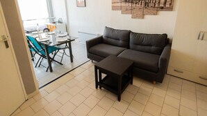 Ein Wohnzimmer mit einem dunkelgrauen Sofa, einem kleinen Tisch und einem Essbereich mit Tisch und Stühlen.