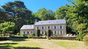 Un bâtiment en pierre doté d’une façade symétrique, de nombreuses fenêtres et d’une pelouse bien entretenue agrémentée de quelques arbres.