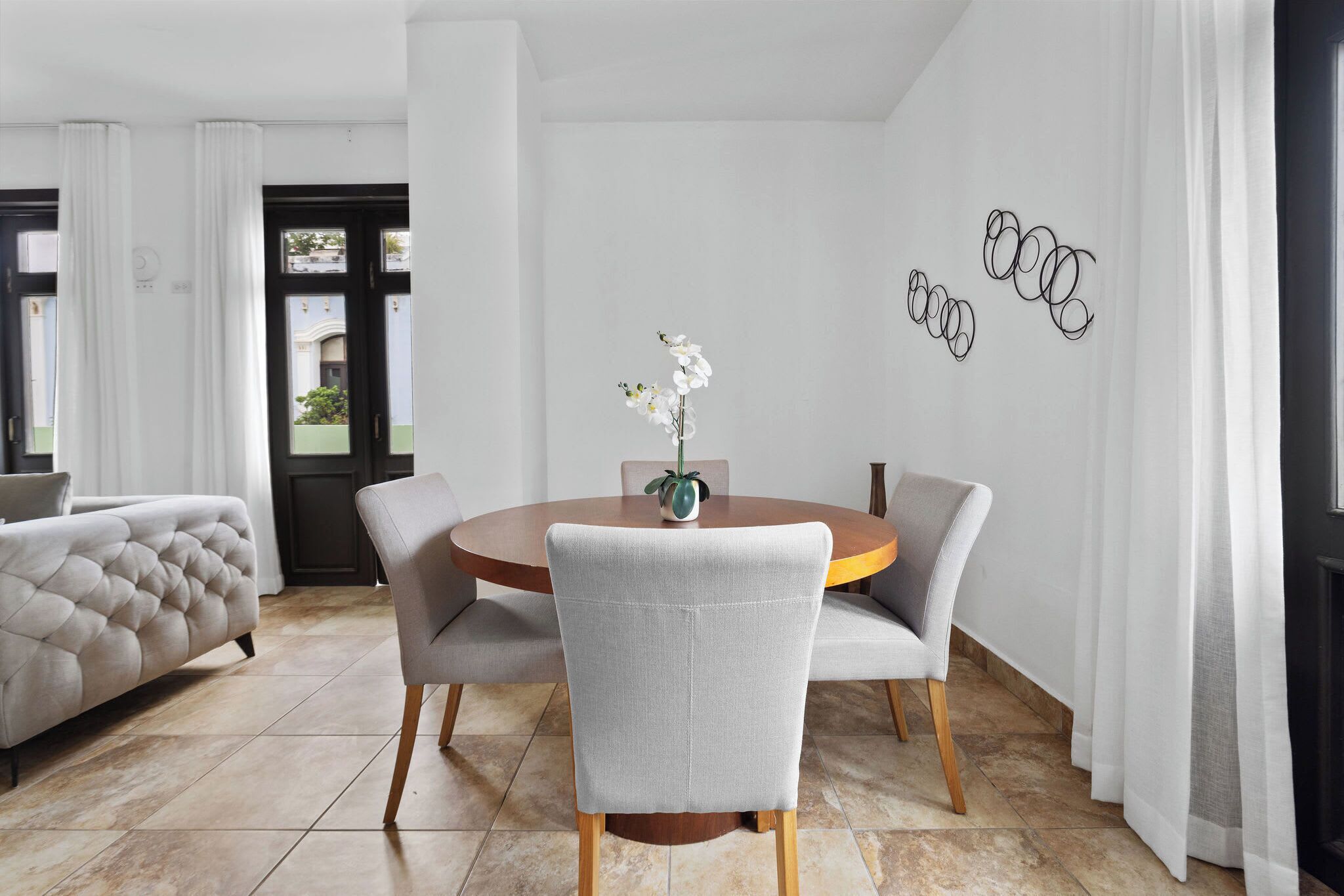 A modern dining area with a round table, grey upholstered chairs, and a vase with white flowers.