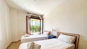 Une chambre d’hôtel avec deux lits, une fenêtre avec des rideaux, une table de chevet avec une lampe et une vue sur la verdure à l’extérieur.