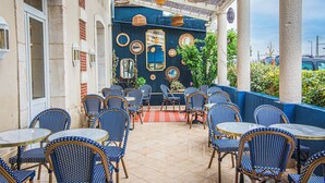 Um café ao ar livre com cadeiras e mesas de padrão azul, espelhos decorativos e luminárias pendentes de vime.