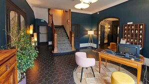 Um saguão de hotel com escada, uma mesa de atendimento com computador, uma área de estar e uma exposição de prêmios.
