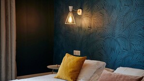 Quarto com uma cama, mesa de cabeceira e luminária na parede.