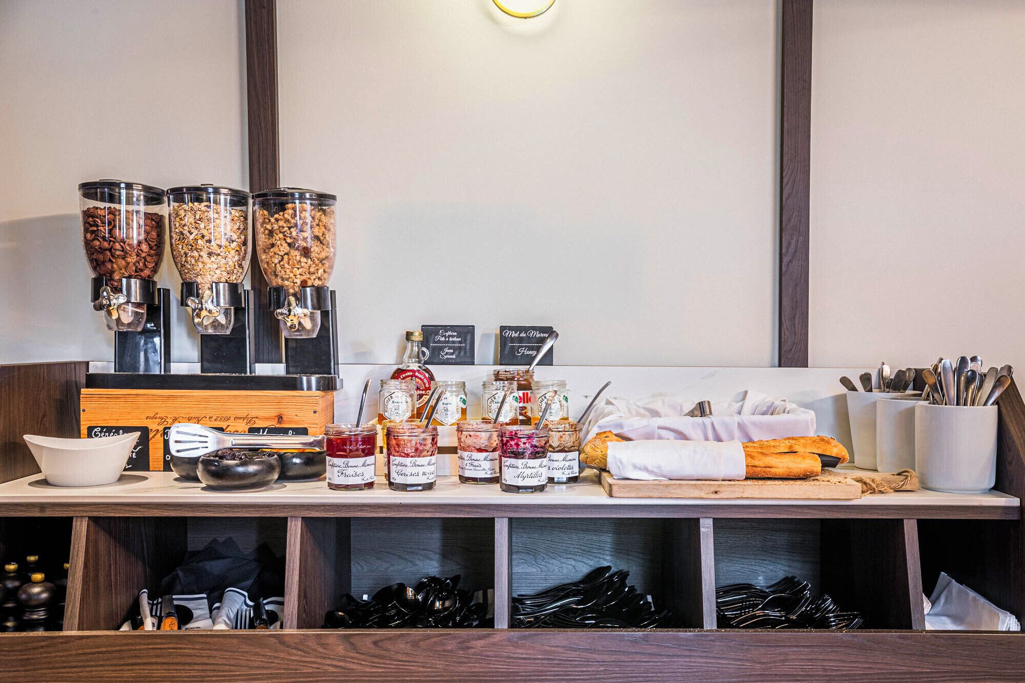 A breakfast bar with coffee dispensers, jars of spreads, and utensils.