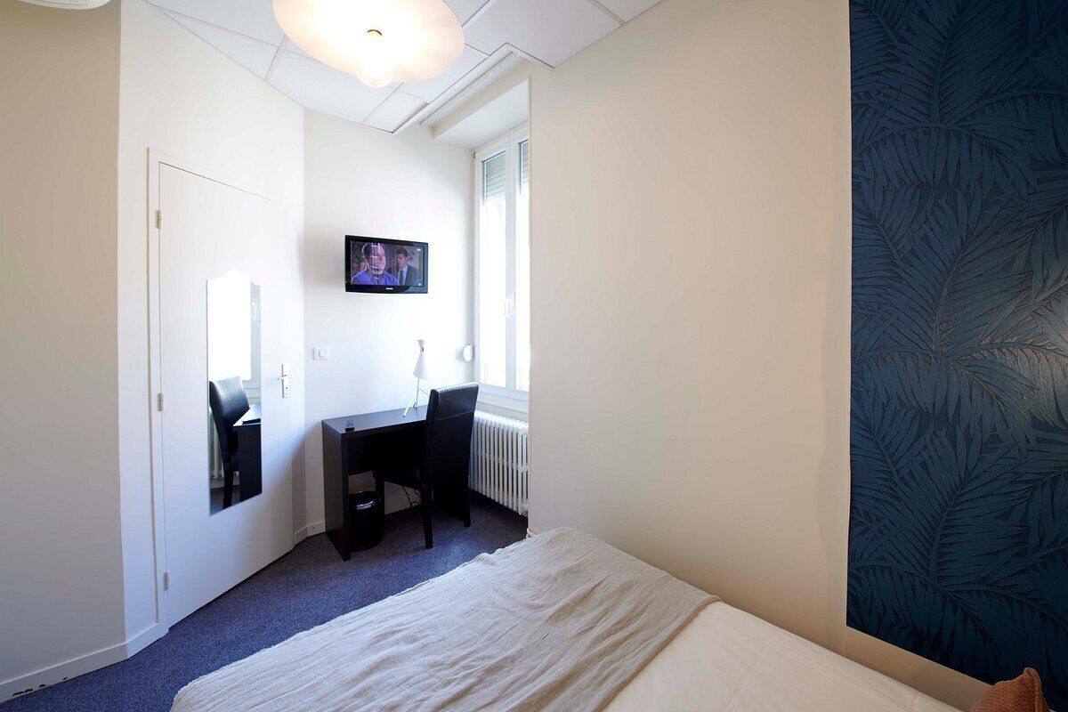 A bedroom with a bed, a desk, a chair, a television, and a window.