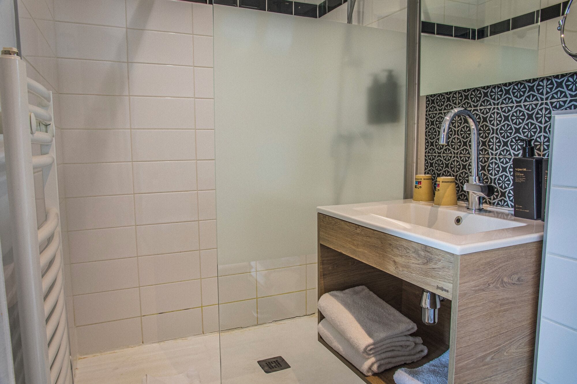 A bathroom with a white sink, wooden vanity, and a shower area.