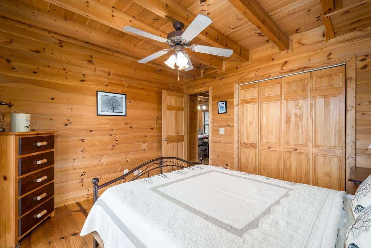 A wooden cabin bedroom with a bed, a dresser, a ceiling fan, and wooden walls.