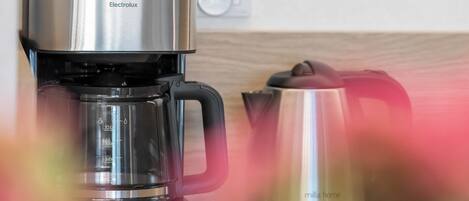 Una cafetera con acabado metálico y jarra de vidrio, sobre una superficie de madera.
