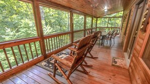 A wooden deck with rocking chairs and a table, overlooking a forested area. - Black Bear Lodge Summ (Blue Ridge)