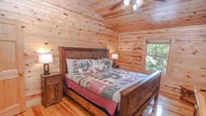 A wooden cabin bedroom with a bed, two bedside lamps, a nightstand, and a window. - Black Bear Lodge Summ (Blue Ridge)