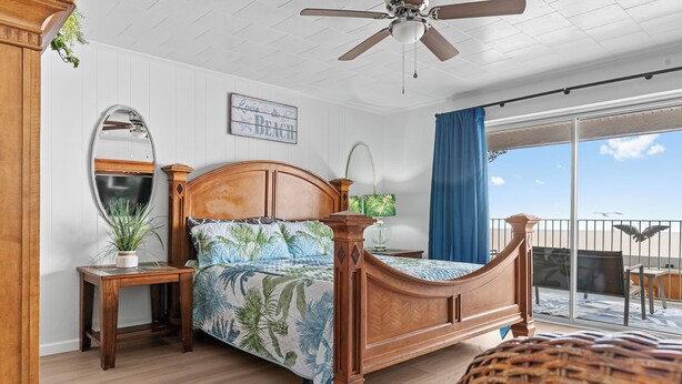 A bedroom with a wooden bed, a nightstand, a mirror, a potted plant, and a view of the balcony.