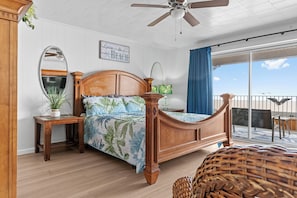 A bedroom with a wooden bed, a nightstand, a mirror, a potted plant, and a view of the balcony.