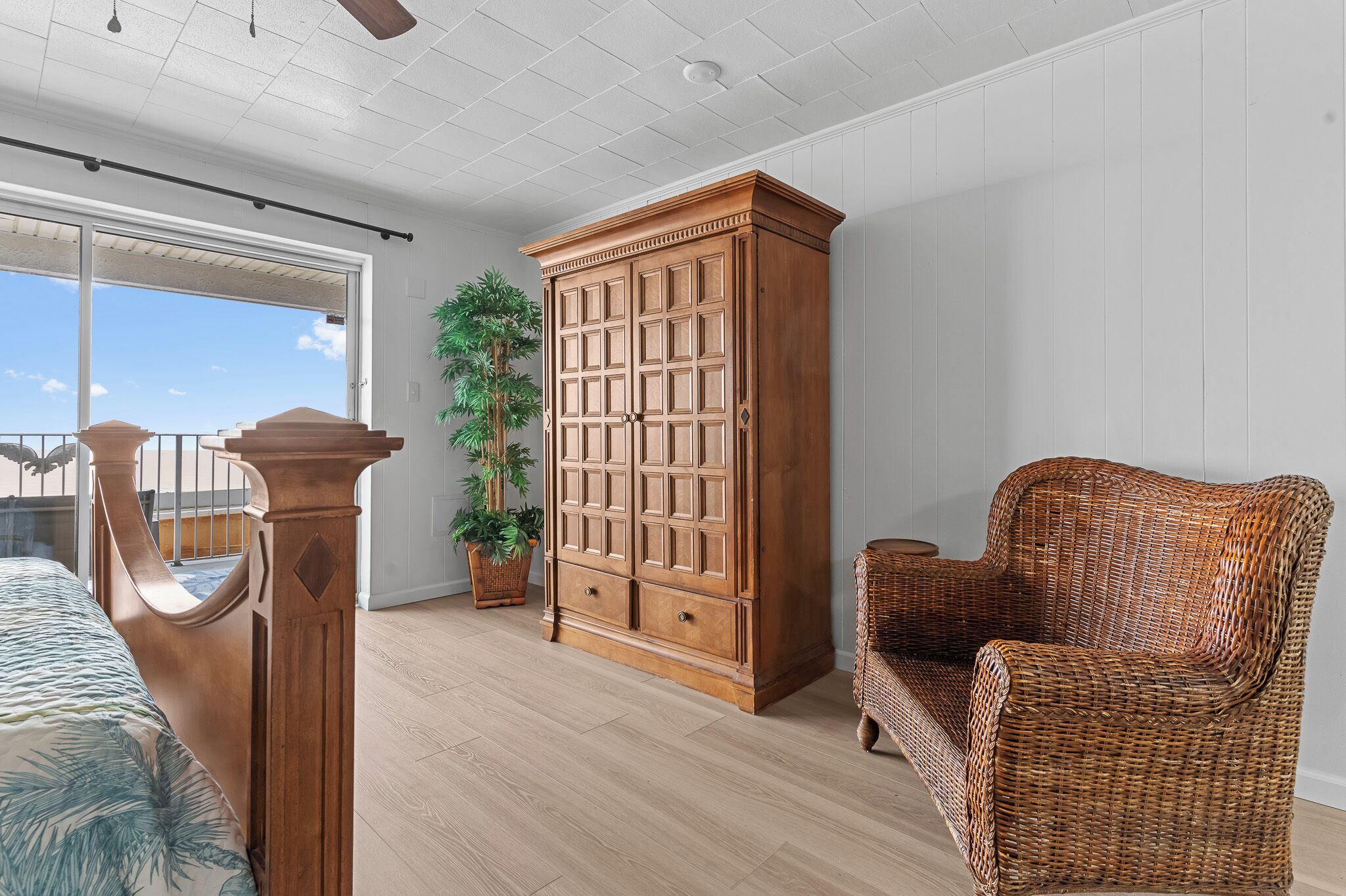 Une pièce comprenant un lit, une armoire en bois, une chaise en osier et une plante en pot.
