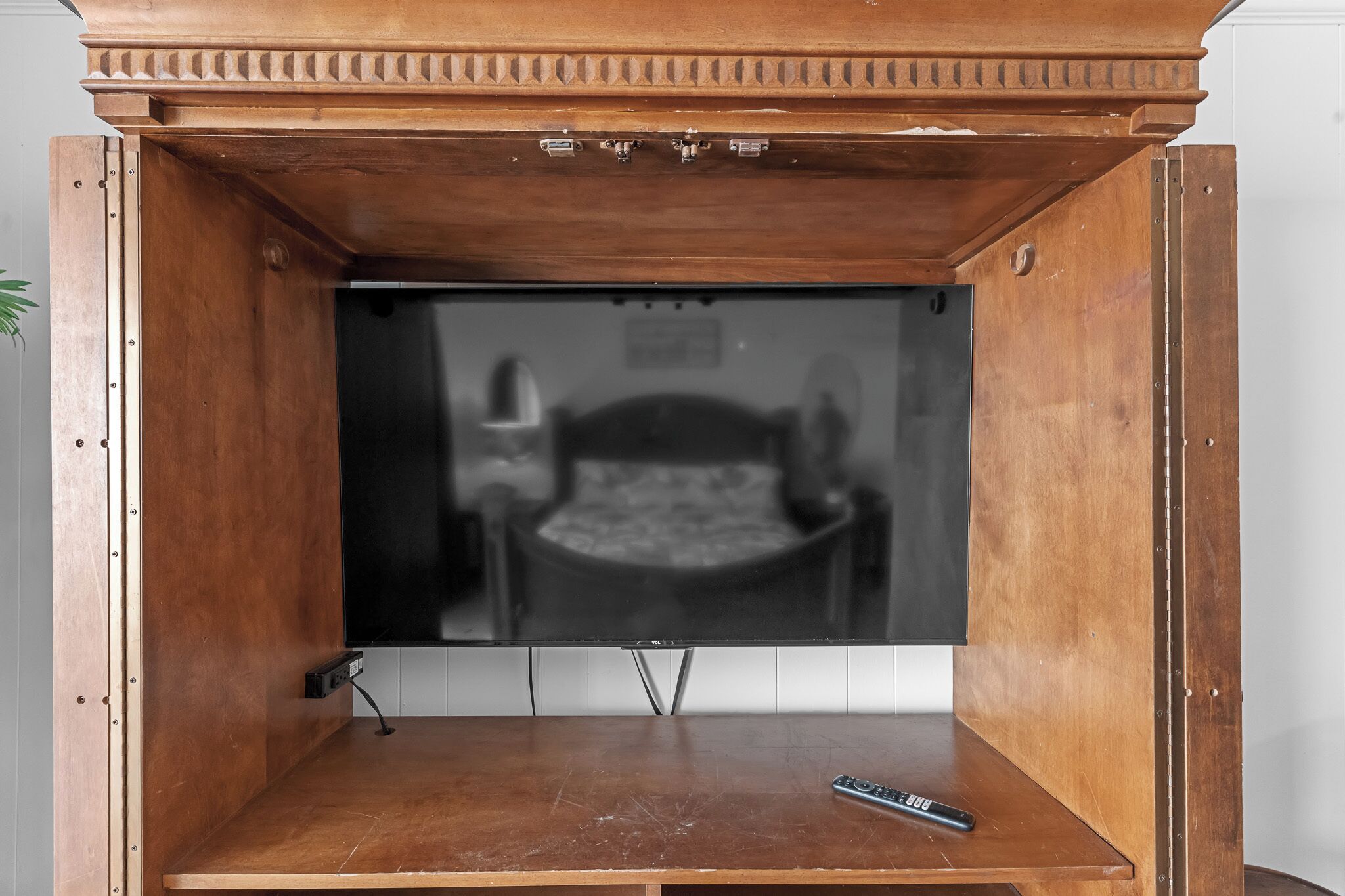 Un mueble bajo de madera para televisor con un televisor de pantalla plana, un control remoto y un enchufe.