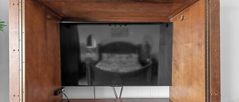 Un mueble bajo de madera para televisor con un televisor de pantalla plana, un control remoto y un enchufe.