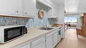 A kitchen with white cabinets, a microwave, a sink, and a stove. There is a wicker basket on the wall and a view of the outside through a glass door.