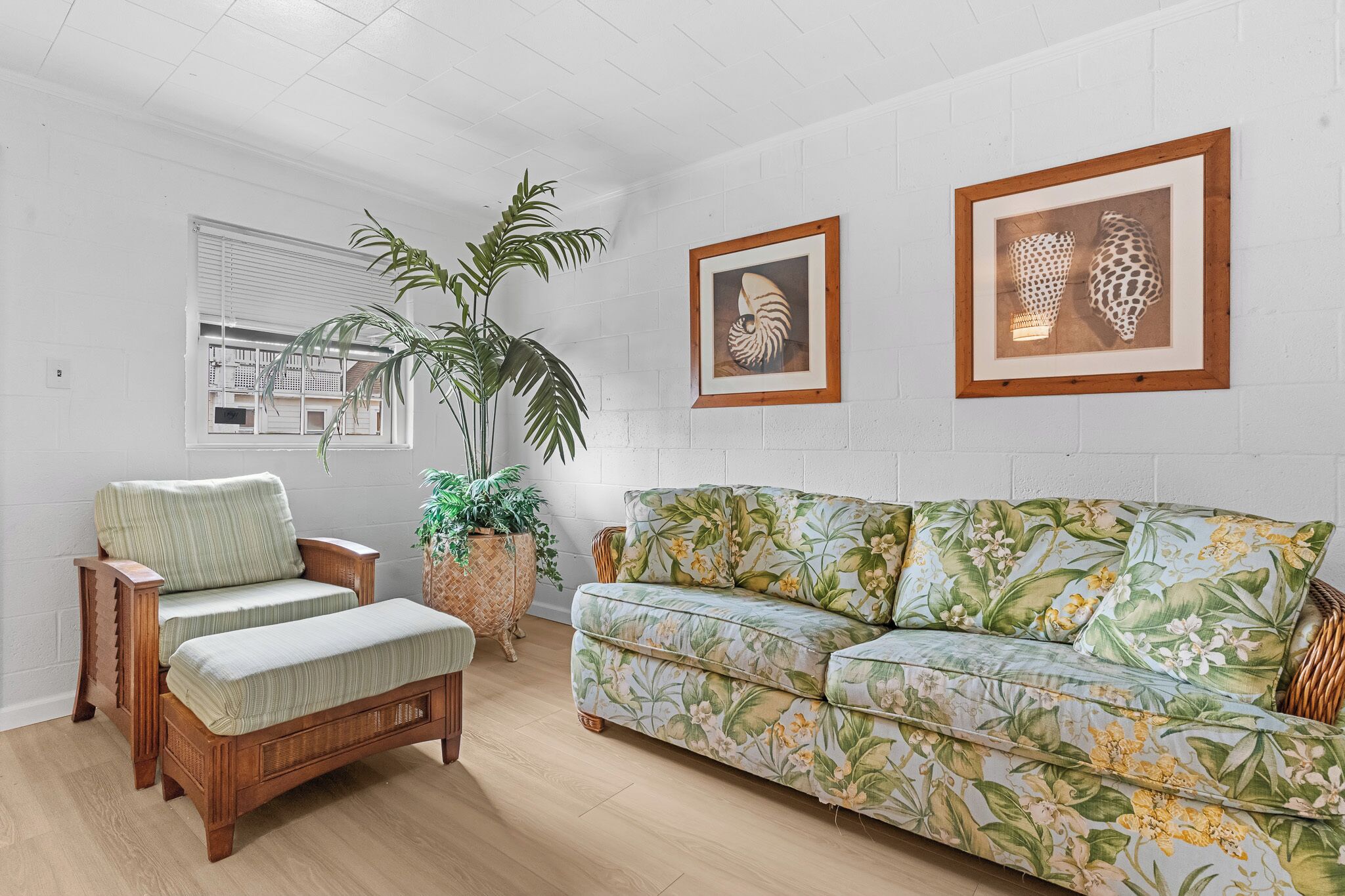 Ein Wohnzimmer mit einer Couch, einem Sessel, einer Bank, einer Topfpflanze und gerahmten Kunstwerken an der Wand.
