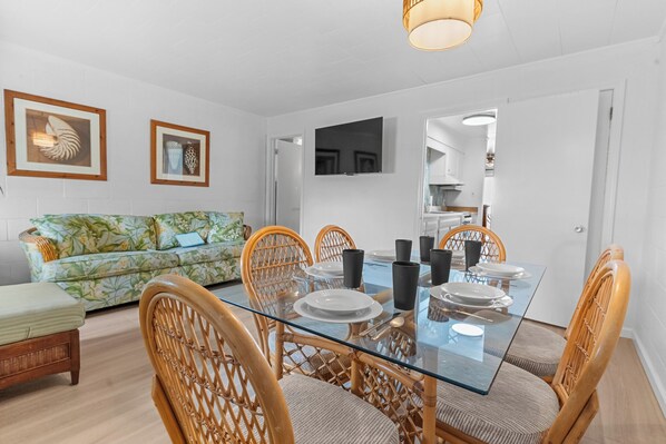 A dining area with a glass table, wicker chairs, and a floral sofa.