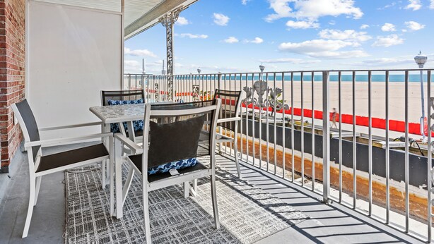 A balcony with a view of the beach, a table with chairs, and a railing. - 2 Bed/1 Bath on the Boardwalk by the Inlet (Ocean City)