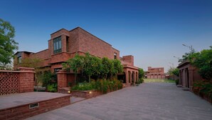 A modern building with a brick facade, a central courtyard, and surrounding greenery. - TreeHouse Rajbagh (Luni)