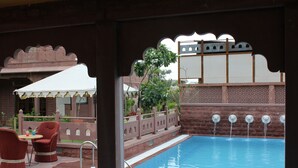 A pool area with a white canopy, red chairs, and a brick wall with decorative elements. - TreeHouse Rajbagh (Luni)