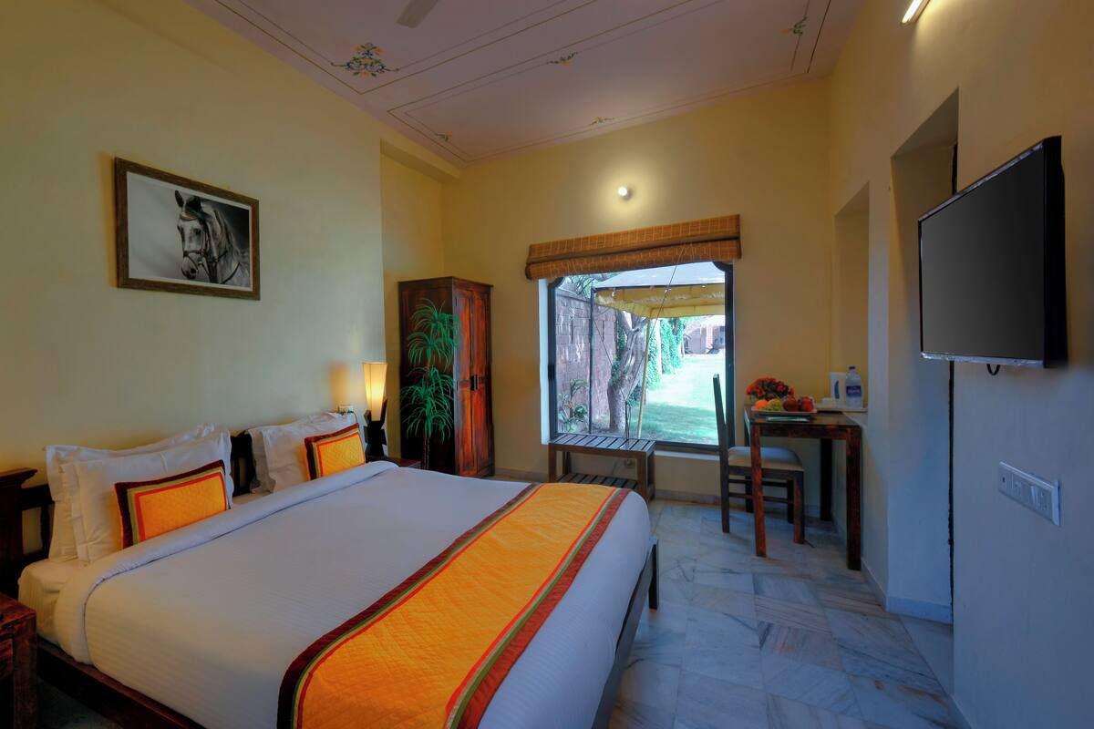 A hotel room with a large bed, a desk with a chair, a television, and a window with a view of the outdoors.