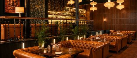 A restaurant with leather booths, a bar area, and hanging lantern-style lights.