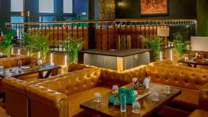 A restaurant with leather booths, hanging lamps, and a large painting on the wall. - TreeHouse Rajbagh (Luni)