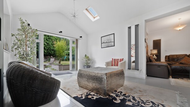 A modern living room with a large glass door leading to a garden, a stone coffee table, a wicker chair, and a leather sofa. - 3 Bedroom Spacious Bungalow Sunningdale Lodge Ascot Racecourse (Sunningdale)