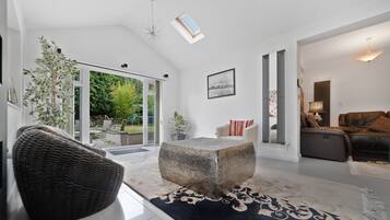 A modern living room with a large glass door leading to a garden, a stone coffee table, a wicker chair, and a leather sofa.