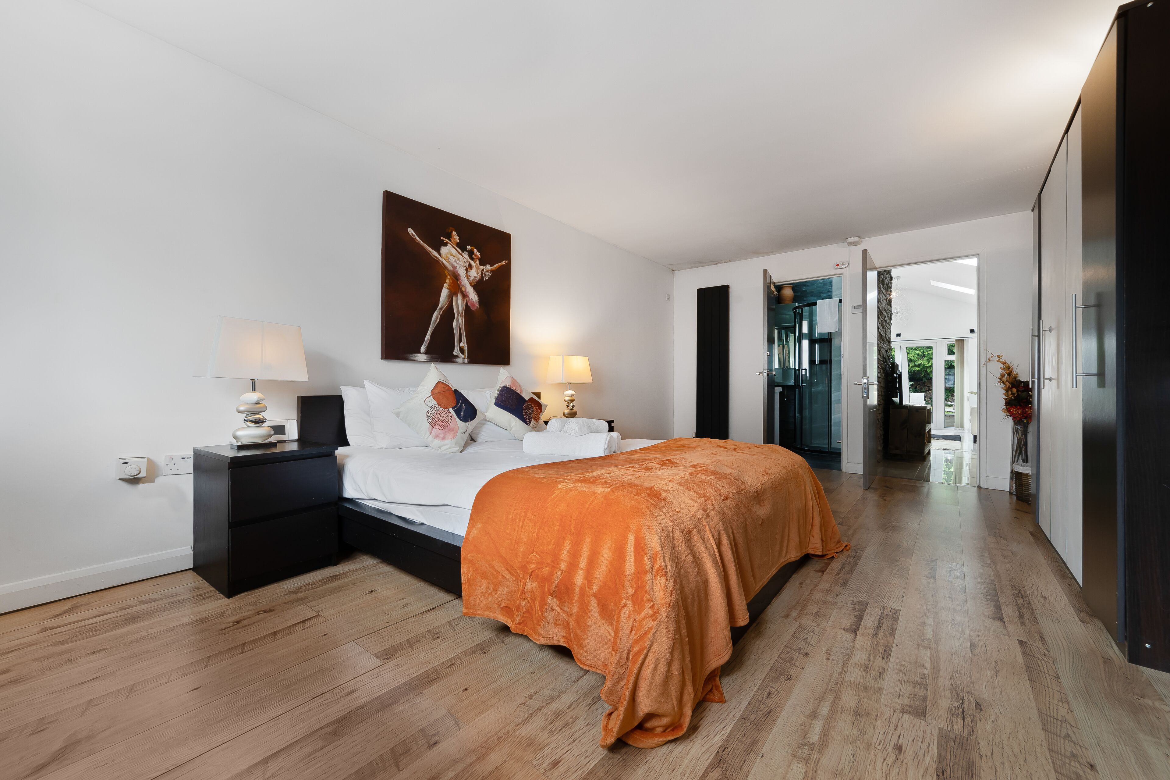 A modern bedroom with a large bed, two bedside tables, a nightstand, and a painting on the wall.