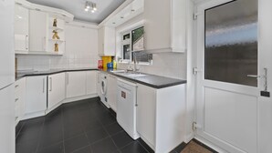 A modern kitchen with white cabinetry, a built-in washing machine, and a large window. - 3 Bedroom Spacious Bungalow Sunningdale Lodge Ascot Racecourse (Sunningdale)