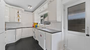 A modern kitchen with white cabinetry, a built-in washing machine, and a large window.