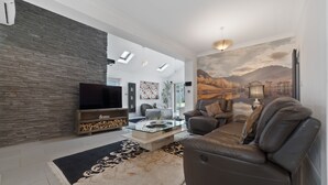 A modern living room with a stone wall, a glass coffee table, a leather sofa, and a mural of a landscape. - 3 Bedroom Spacious Bungalow Sunningdale Lodge Ascot Racecourse (Sunningdale)