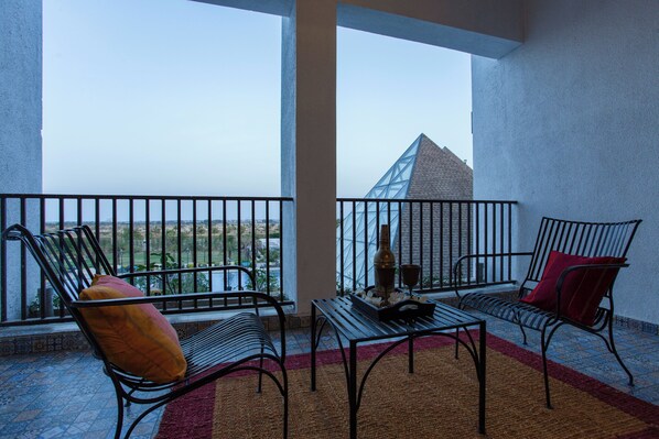 A balcony with two metal chairs, a table, and a view of a pyramid-like structure.